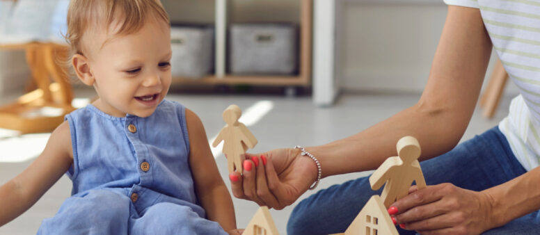 Kind spielt mit Mama auf dem Teppich mit Holzspielzeug